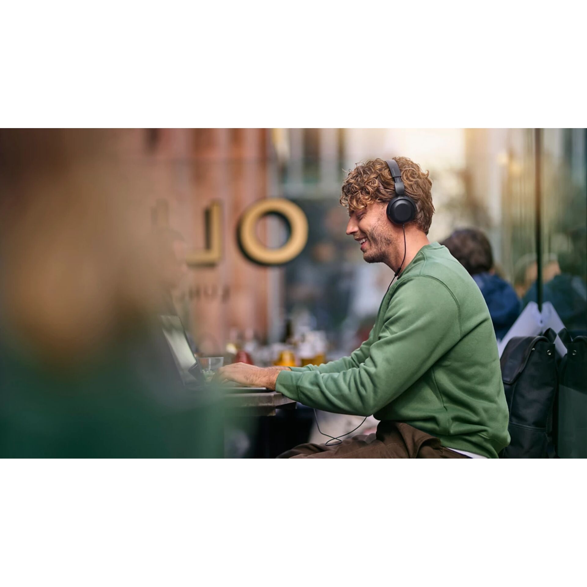 Kopfhörer, grünes Sweatshirt, Laptop, Außen-CCafe, lockiges Haar